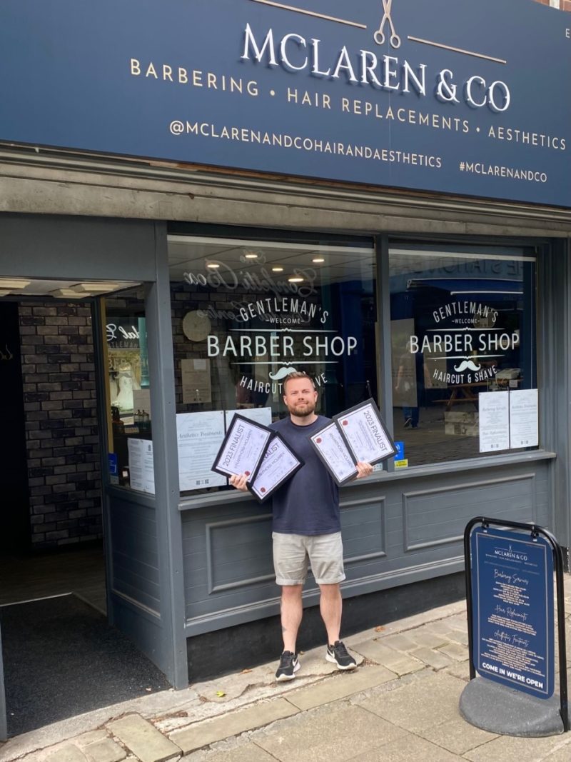 A photo of Ian standing outside his business holding his 4 finalist certificates